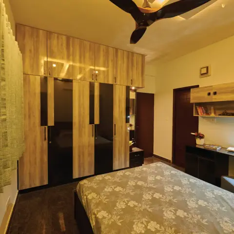 Bedroom whose wardrobe run alternates driftwood-laminate and black lacquered-glass shutters