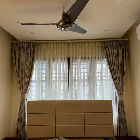 Bedroom window with double-layer sheer and textured drapes with tiebacks, above a tufted panel upholstered headboard.