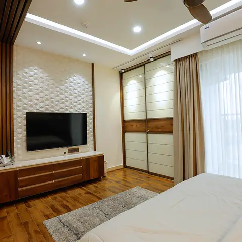 Bedroom with a 3D geometric textured accent wall behind a wood TV console, a sliding-door wardrobe, and sheer curtains opening to a balcony.