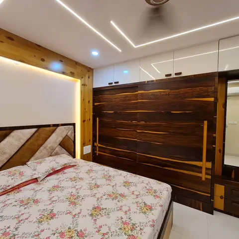 Bedroom with a backlit pine accent wall behind a diagonal-tufted headboard and a dark walnut-finish sliding wardrobe with mirror unit.