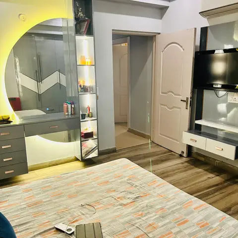 Bedroom with a backlit round mirror dressing unit and lit vertical display shelving, a grey chevron-pattern wardrobe reflected behind it
