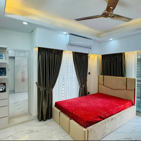 Bedroom with a beige channel-tufted bed dressed in a red satin sheet, olive silk drapes with tie-backs, and a cove-lit tray ceiling.