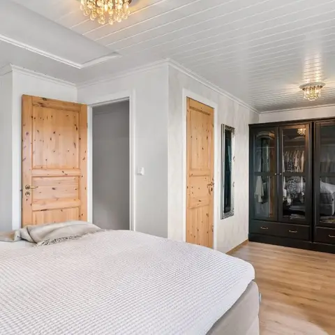 Bedroom with a black glass-front wardrobe, a wood-plank ceiling, a crystal chandelier, and a mirrored dresser topped with a decorative horse bust lamp.
