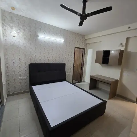 Bedroom with a black tufted-headboard bed on a bare mattress board, floral wallpaper accent wall, and a study desk with wall-mounted cabinet in the corner