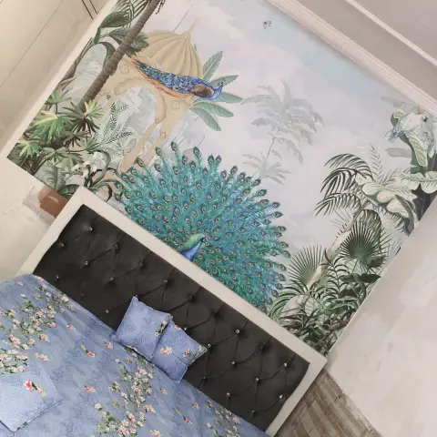 Bedroom with a black tufted upholstered headboard, blue floral bedding, and a large-scale peacock and palm mural wallpaper feature wall.