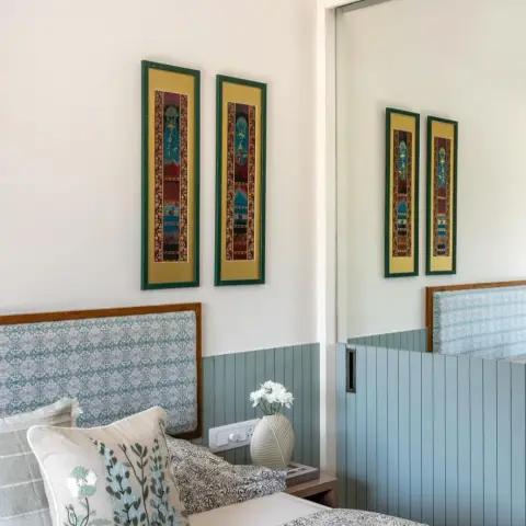 Bedroom with a block-print upholstered headboard, sage-green vertical wood wainscoting and framed traditional Indian miniature art on the wall.