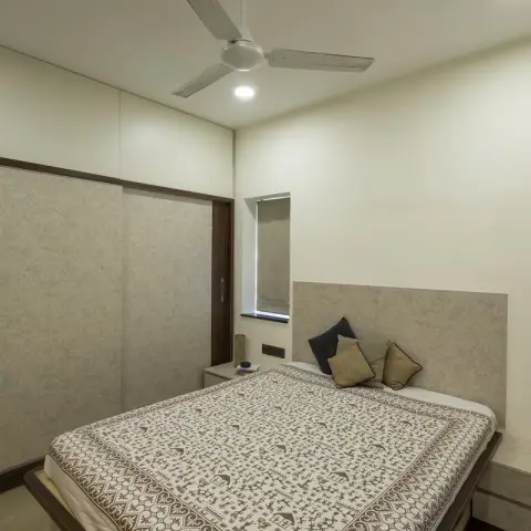Bedroom with a block-printed cream bedspread on a low bed, a grey textured headboard panel running into a wall-hung side console