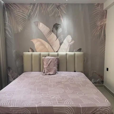 Bedroom with a blush tropical-leaf wallpaper mural filling the wall behind a wide cream channel-tufted headboard