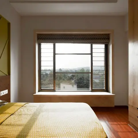 Bedroom with a bold olive-green geometric panel headboard wall, a built-in window seat under a large barred window with woven blinds, wood flooring