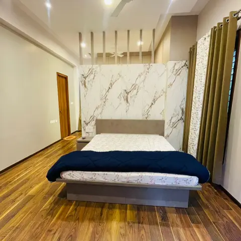 Bedroom with a book-matched white marble-look slab wall behind a low concrete-finish platform bed, olive eyelet curtains over floral sheers