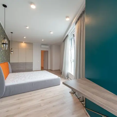 Bedroom with a botanical-print wallpaper accent wall, orange-backed grey daybed, and a teal feature wall beside the window.