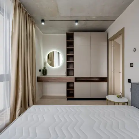 Bedroom with a built-in wardrobe and open-shelf dressing nook featuring a backlit round mirror, exposed concrete ceiling
