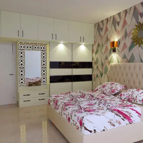Bedroom with a buttoned cream headboard against a pastel geometric chevron wallpaper, flanked by amber-shade sconces and a gilt sunburst mirror