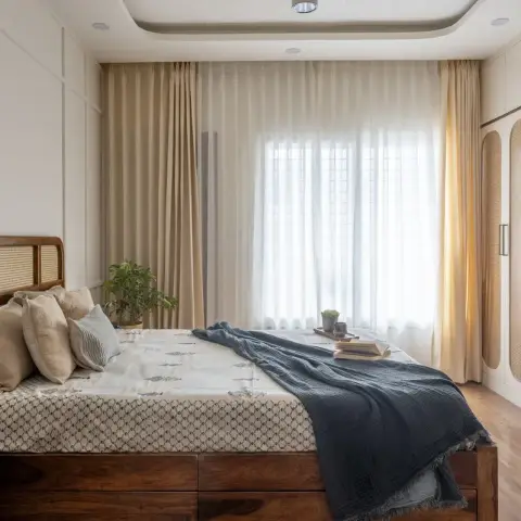 Bedroom with a cane-panel teak headboard and block-printed bedding, a charcoal muslin throw across the foot
