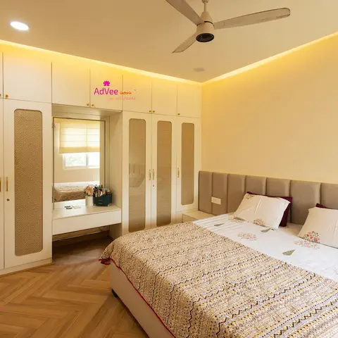 Bedroom with a cane-pattern white wardrobe wall wrapping a mirrored dressing nook, a herringbone wood floor, and a beige tufted upholstered headboard.