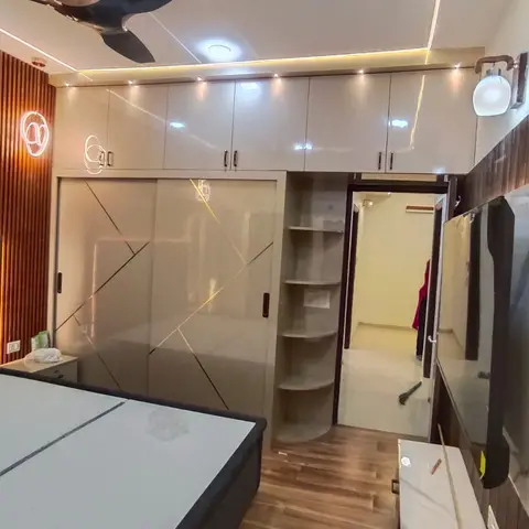 Bedroom with a champagne-gold sliding-door wardrobe featuring angular gold-line inlays, a cove-lit box ceiling, a round illuminated wall decor niche