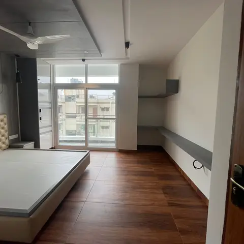 Bedroom with a champagne tufted platform bed, wood-look tile flooring and a plain grey ledge shelf leading to a balcony.