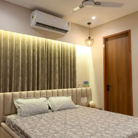 Bedroom with a channel-tufted beige upholstered headboard backed by textured curtains and a backlit cove niche, a wire-cage pendant light