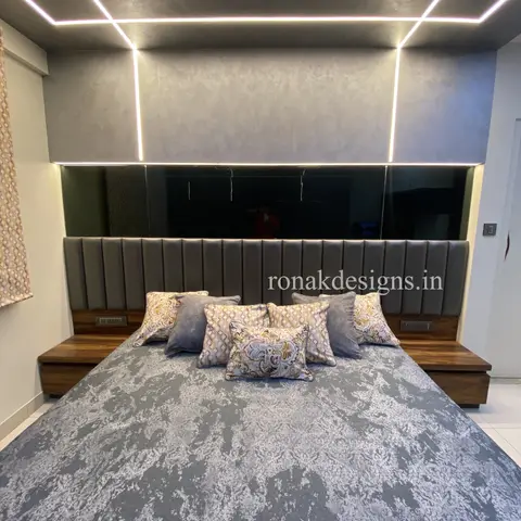 Bedroom with a channel-tufted grey upholstered headboard wall, a mirrored accent strip above, a backlit rectangular LED ceiling frame
