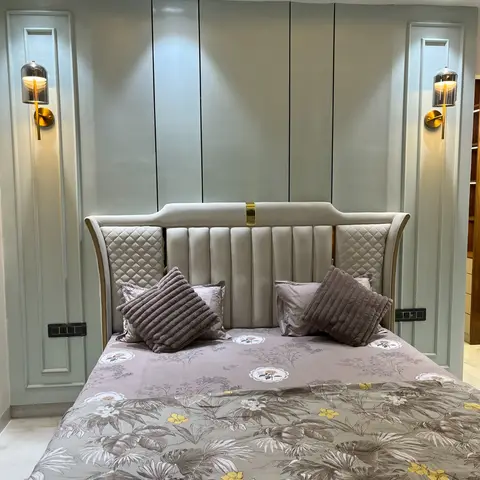 Bedroom with a channel-tufted grey upholstered headboard flanked by diamond-quilted wings and a brass accent strip