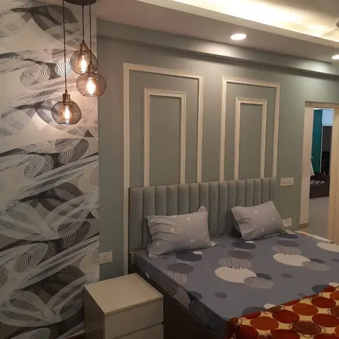 Bedroom with a channel-tufted grey headboard against a sage wall with picture-frame moulding, beside a black-and-white patterned wallpaper wall.