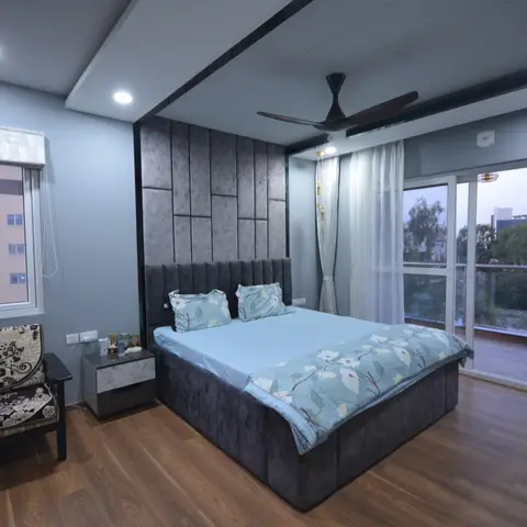Bedroom with a channel-tufted grey upholstered headboard wall, a floral-cushioned accent chair by the window