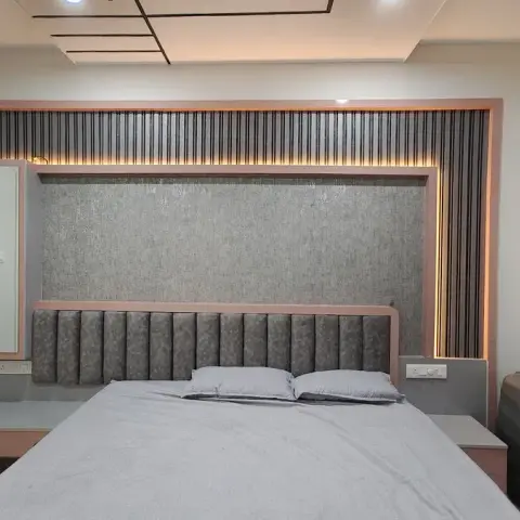 Bedroom with a channel-tufted grey headboard framed in pink trim, a backlit vertical-fluted panel wall, a wall-mounted mirror, and a sunburst wall clock