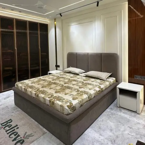 Bedroom with a channel-tufted taupe upholstered bed, raised panel moulding on the headboard wall, cove ceiling lighting, and a fluted bronze-glass wardrobe