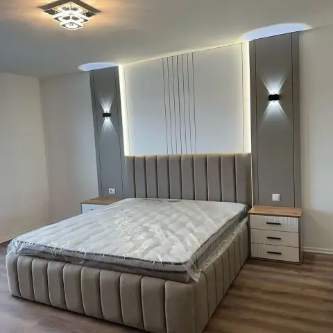 Bedroom with a channel-tufted upholstered bed against a backlit vertical-slat panel wall, flanked by symmetrical tall grey wardrobes and up-down wall sconces