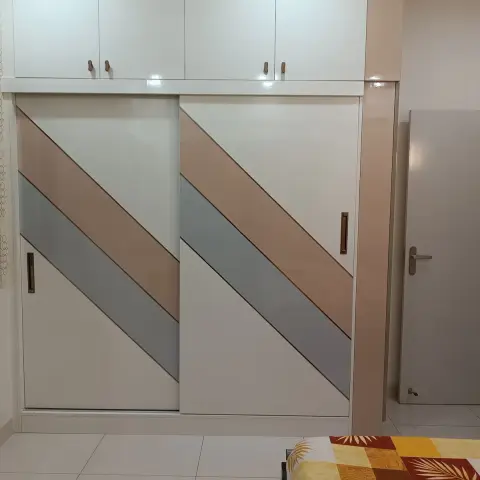 Bedroom with a color-blocked sliding-door wardrobe in diagonal peach and grey stripes, glossy white overhead cabinets