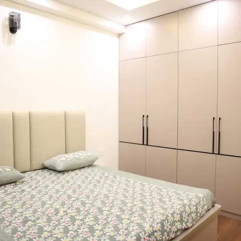 Bedroom with a cream vertically-channelled upholstered headboard, a single perforated-metal lantern sconce above it