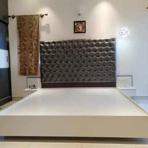 Bedroom with a crystal-studded silver tufted headboard, a floating white platform bed base, and a dark glass-shutter wardrobe beside a geometric pendant light.