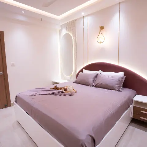 Bedroom with a curved wine-red upholstered headboard, gold-lined wall panelling, and a backlit oval mirror beside the bed