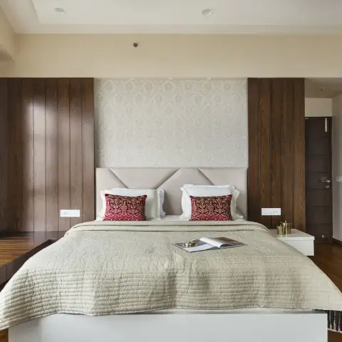 Bedroom with a damask wallpaper panel above an upholstered geometric headboard, flanked by dark walnut vertical-groove panelling and a mirrored sliding