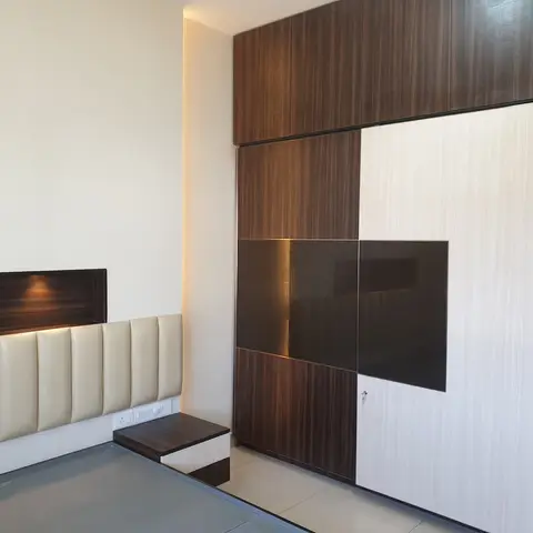Bedroom with a dark-and-light wood sliding wardrobe wall and a channel-tufted cream headboard lit by two recessed cove lights above it.