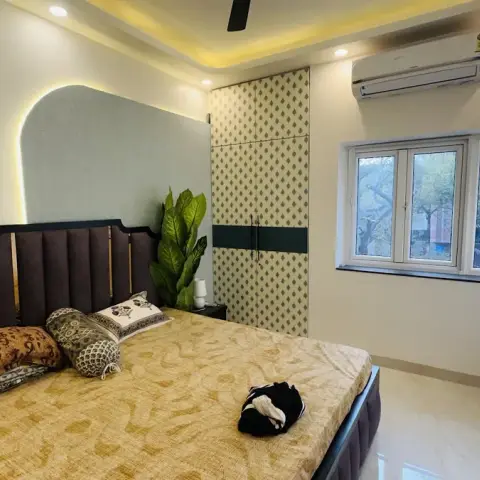 Bedroom with a dark tufted upholstered headboard against an arched backlit panel, a patterned wardrobe with dark banding and a mustard bedspread