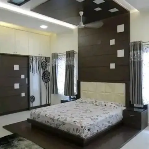 Bedroom with a dark wood accent wall carrying square white inlays up onto a cove-lit POP false ceiling, a quilted cream headboard