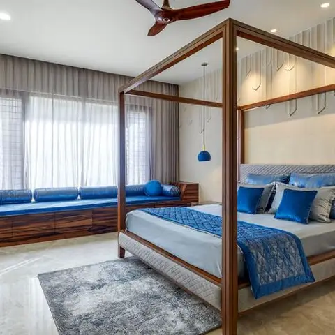 Bedroom with a dark wood four-poster canopy bed dressed in blue and grey quilted bedding, a matching built-in blue window seat with storage drawers