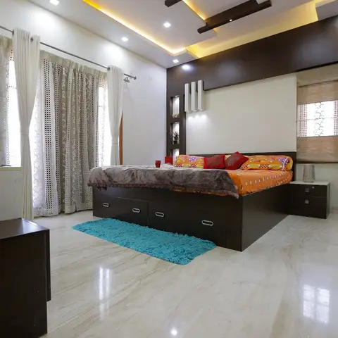 Bedroom with a dark wood storage bed against an upholstered headboard wall with vertical niche lighting, orange and red bedding, teal rug