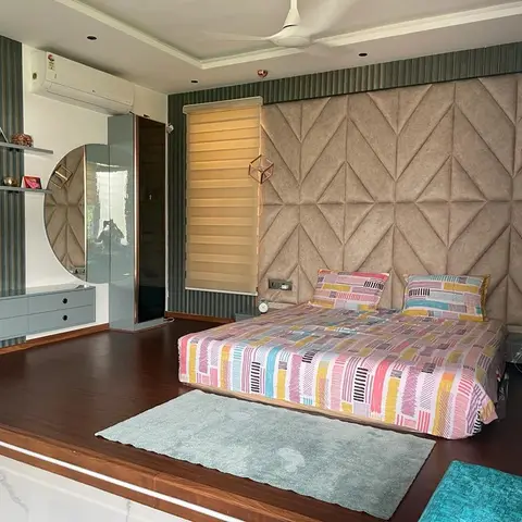Bedroom with a diamond-tufted taupe fabric headboard wall, a colourful patchwork-print bedspread on a raised wood platform