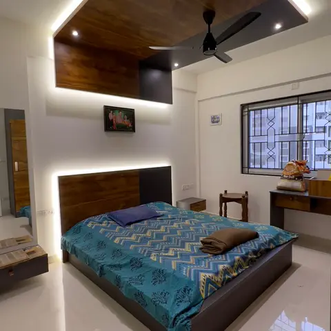 Bedroom with a dramatic wood-clad false-ceiling drop with LED cove lighting above a wood-and-black headboard bed, a small wall-mounted study desk