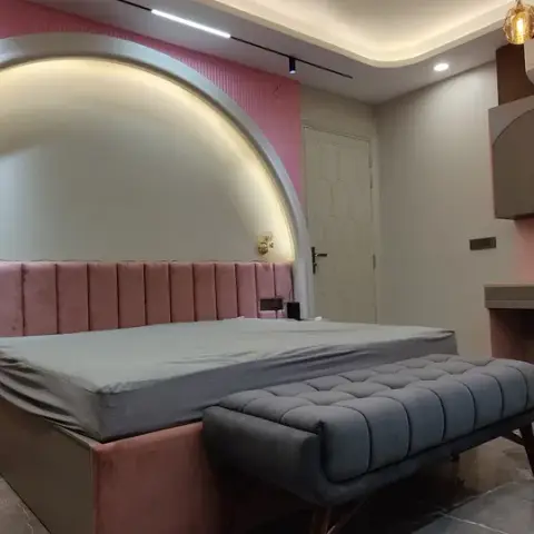 Bedroom with a dusty-pink fluted feature wall and a backlit white arch framing a channel-tufted pink velvet headboard, two small brass sconces on the arch