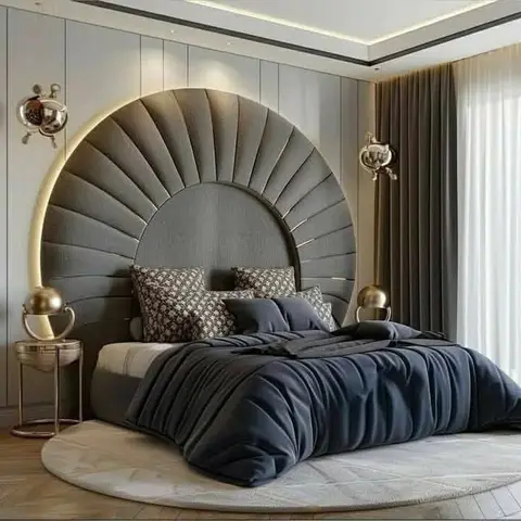 Bedroom with a fan-shaped channel-tufted grey headboard framed by a backlit halo arch and brass globe wall sconces, set on a round rug.