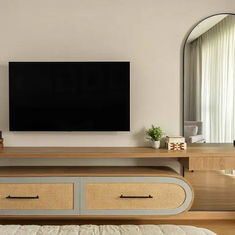 Bedroom with a floating wood TV console featuring rattan cane-front drawers that extends into a dressing table with an arched mirror and styled cosmetics tray.