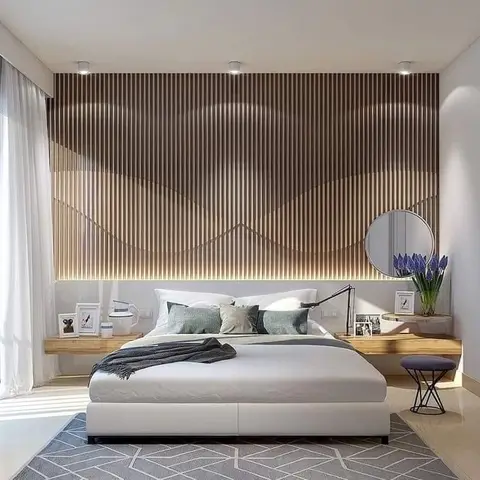 Bedroom with a floor-to-ceiling wavy wood-slat feature wall lit from behind, floating wood nightstand shelves, a round mirror, a white platform bed