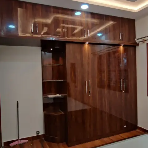 Bedroom with a floor-to-ceiling glossy wood-finish wardrobe with mirrored panels under an angular cove-lit POP false ceiling