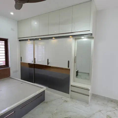 Bedroom with a floor-to-ceiling sliding wardrobe in grey and bronze-accented glossy shutters, an attached mirrored dresser with drawers, and marble flooring