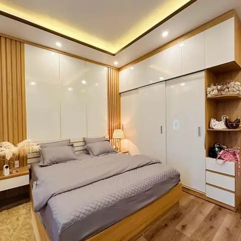 Bedroom with a floor-to-ceiling glossy white wardrobe wall, warm cove ceiling lighting, fluted wood panelling, and an open shelf styled with handbags and shoes.