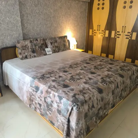Bedroom with a floral-print bedspread on a wood-frame bed, a textured wallpaper accent panel behind the headboard, and a retro-patterned two-tone wardrobe.