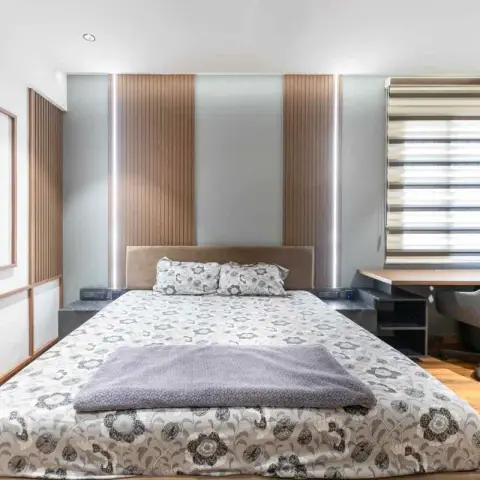 Bedroom with a fluted backlit panel wall behind the headboard and a built-in study desk with open shelving in the corner.